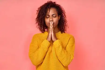 照片中美丽的年轻黑人妇女双手合十祈祷,闭上眼睛,享受祥和的气氛,有